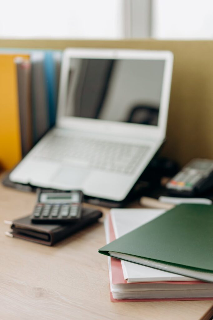 stacks of folder near calculator and laptop on a wooden table